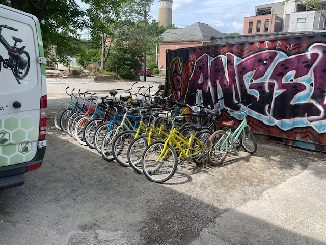 Home 1 A row of bicycles available for Atlanta bike rentals is parked on a dirt lot next to a graffiti-covered shipping container and a white van.